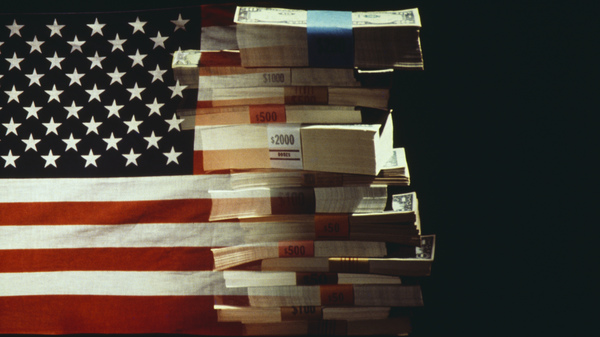 The American flag superimposed over a pile of U.S. dollar bank notes.