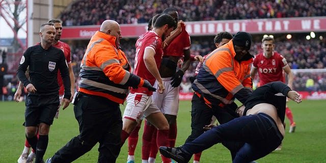 Stewards block a man who invaded the pitch as Nottingham Forest celebrate scoring their side's third goal, during the English FA Cup fourth round soccer match between Nottingham Forest and Leicester City at the City Ground, Nottingham, England, Sunday, Feb. 6, 2022. Police have arrested a man who appeared to attack Nottingham Forest players as they celebrated one of their goals in an FA Cup victory over Leicester. A supporter emerged from the away section of the City Ground before striking out at Forest players as they celebrated the third in a 4-1 win over the cup holders.