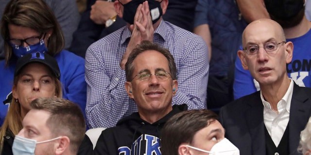Actor and comedian Jerry Seinfeld, center, sits next to NBA Commissioner Adam Silver, right, prior to an NCAA college basketball game between Duke and North Carolina in Durham, N.C., Saturday, March 5, 2022. 