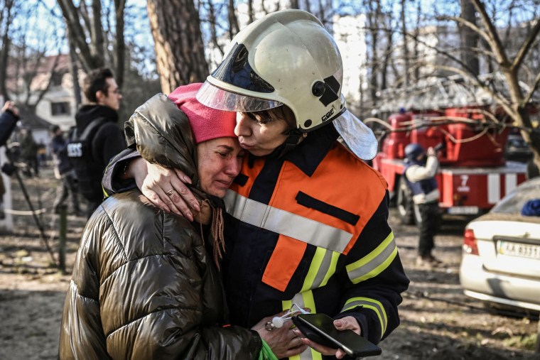 A rescue worker comforts an evacuated resident outside a burning apartment building in Kyiv on March 15, 2022.