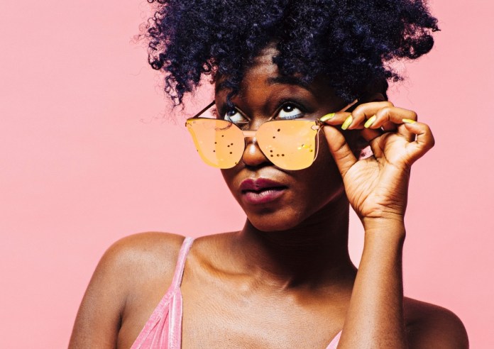 black woman peeking above mirrored sunglasses with a pink background