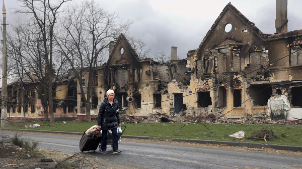 A woman on April 8 pulls her baggage past houses damaged during fighting in Mariupol, Ukraine.