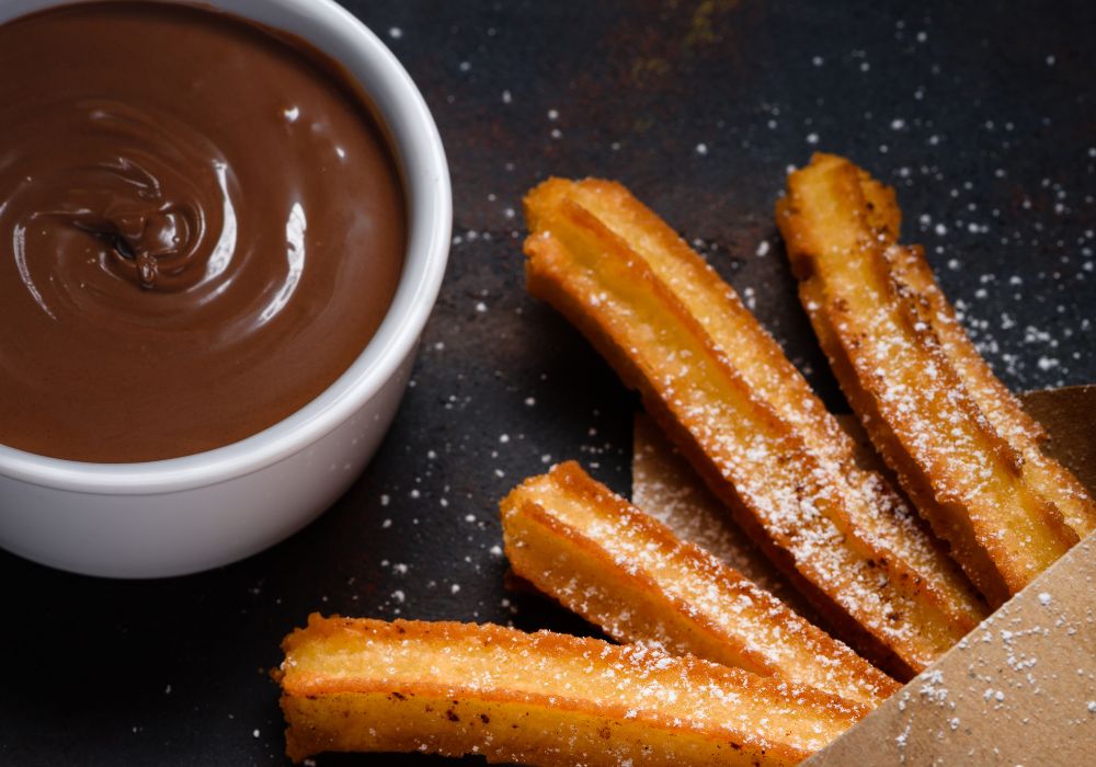 A mouth-watering churros with sugar cinnamon and chocalate sauce dip on dark background.