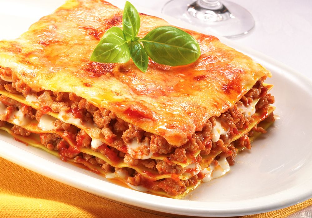 Metaat lasagna with tomato and cheese on a white ceramic plate.