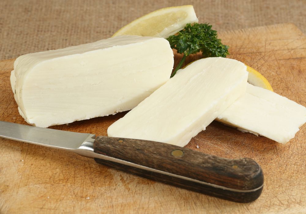 A slice of halloumi cheese on a wooden board with lemon wedges.