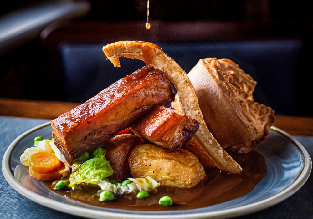 Pouring gravy in a pork belly Sunday roast with pork crackling.