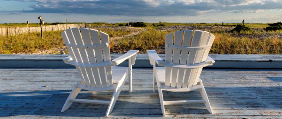 View of beach at Cape Cod, MA with chairs in foreground on a wood deck