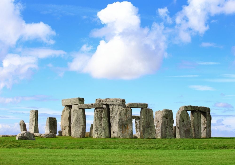 Stonehenge an ancient prehistoric stone monument during daylight on a cloudy blue sky.