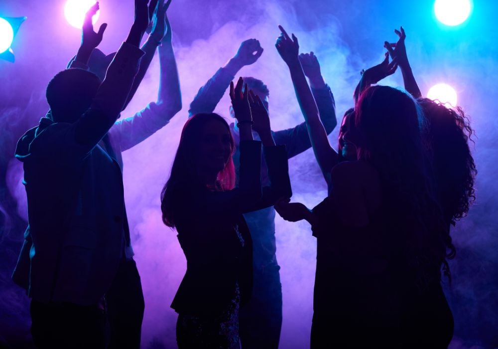 A group of dancing silhouettes of young people in smoke.