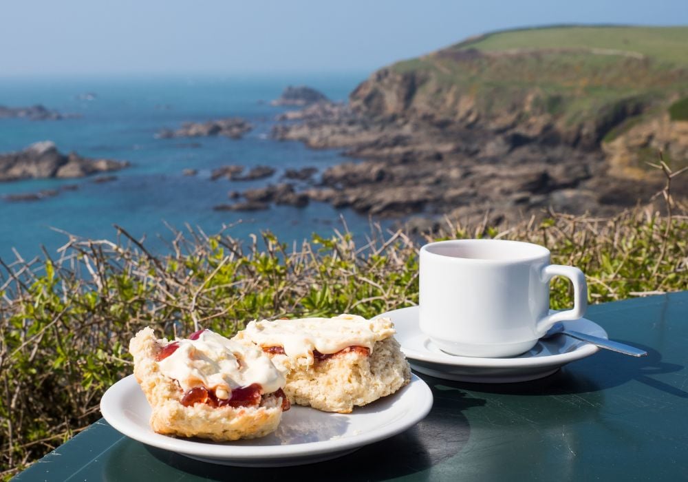 Cornish cream tea, including the scones with jam and clotted cream with a seascape.