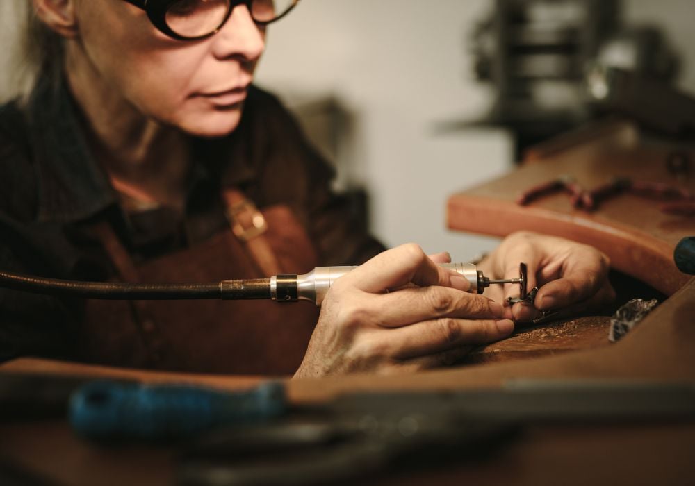Senior female jewelry maker polishing a product at her workbench.