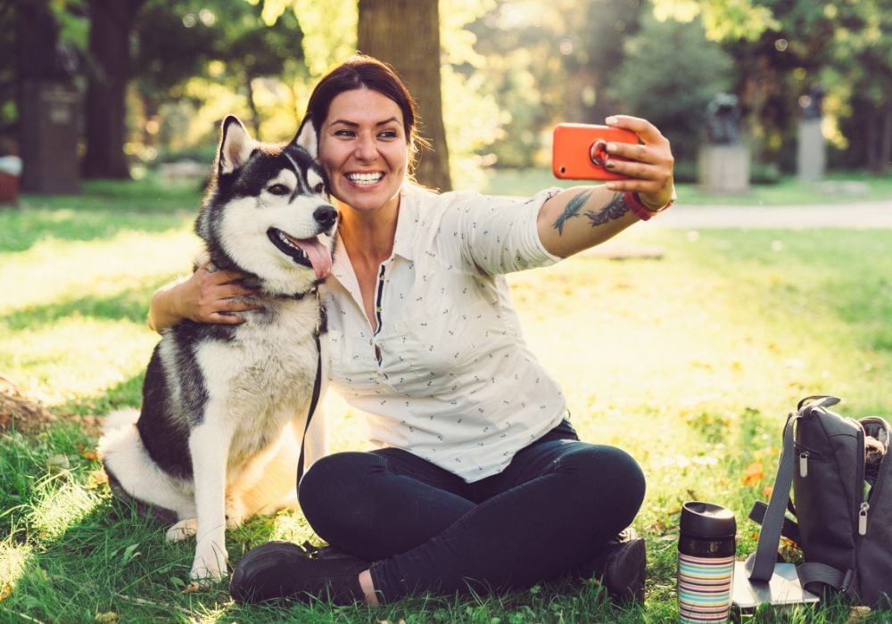 Young woman with her dog taking selfie in the city park