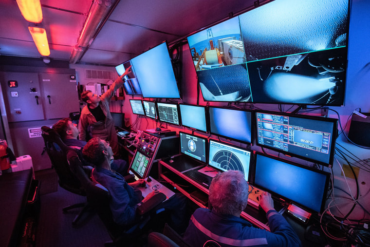 A person points at a monitor on a wall of screens while people work in the PRS Odyssey control room.