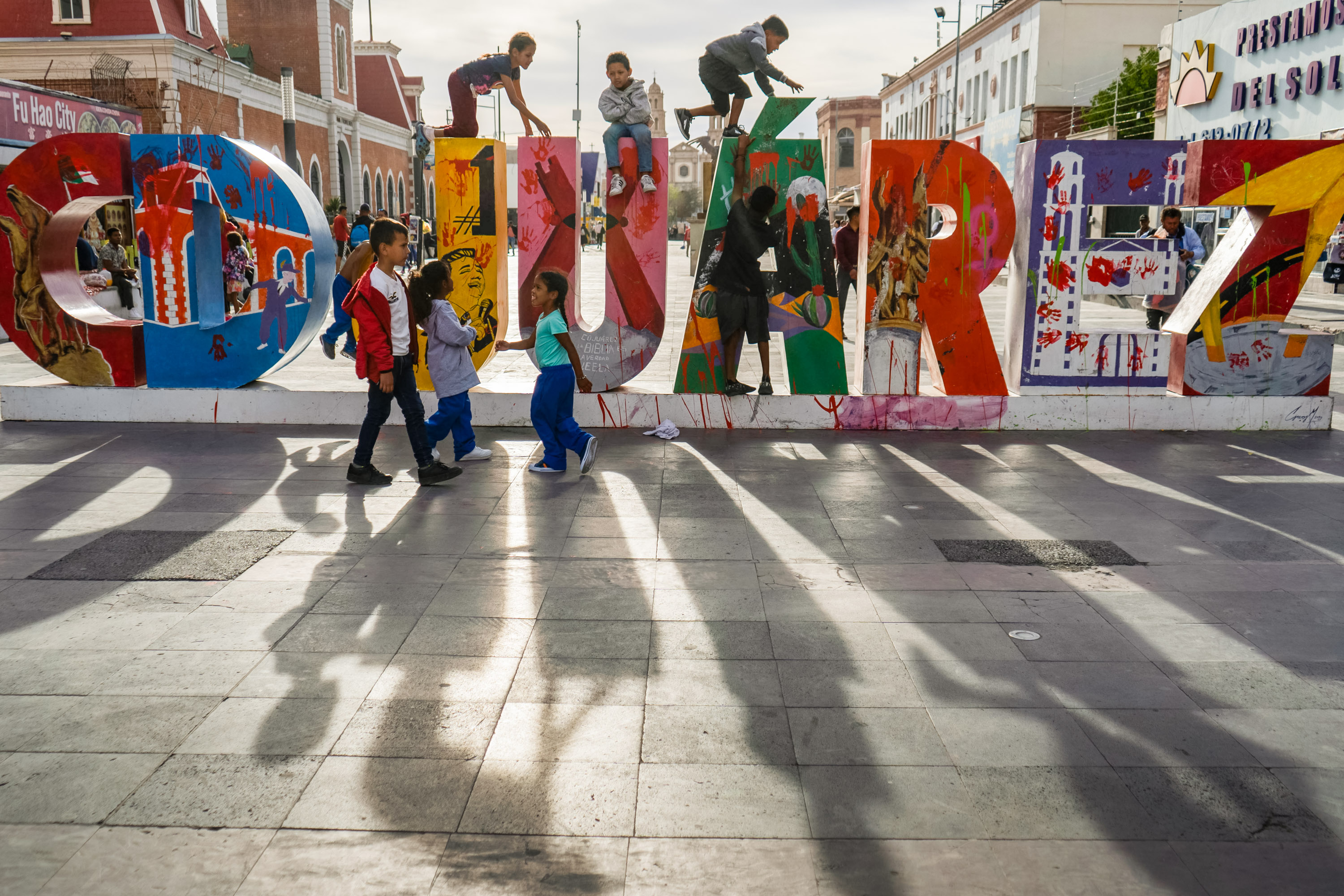 children climb on a 3 dimensional sculpture of the work Juarez. The sun make long shadows into the foreground.