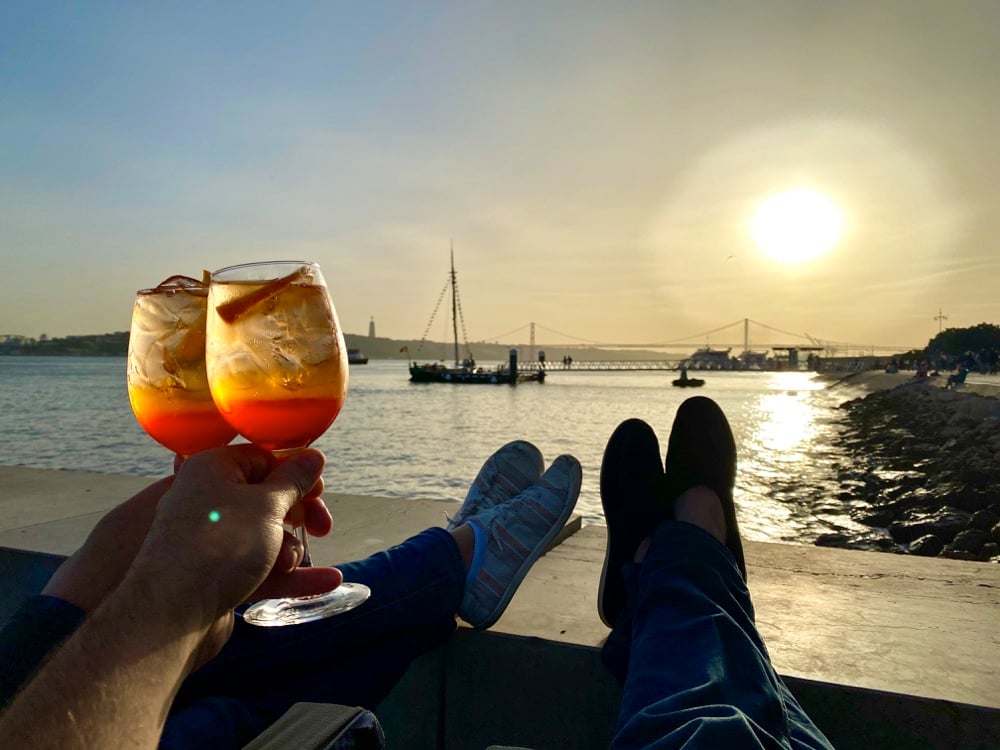 sunset by the water lisbon with a cocktail