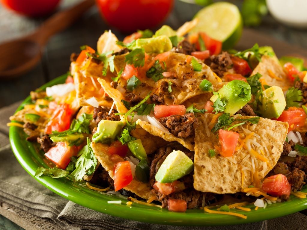 plate of nachos with avocados tomatoes and meat