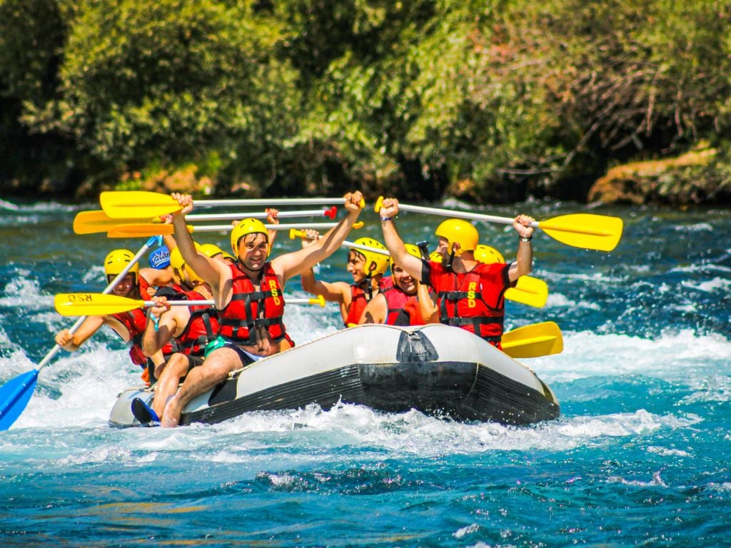 men rafting down a river holding their paddles in the air