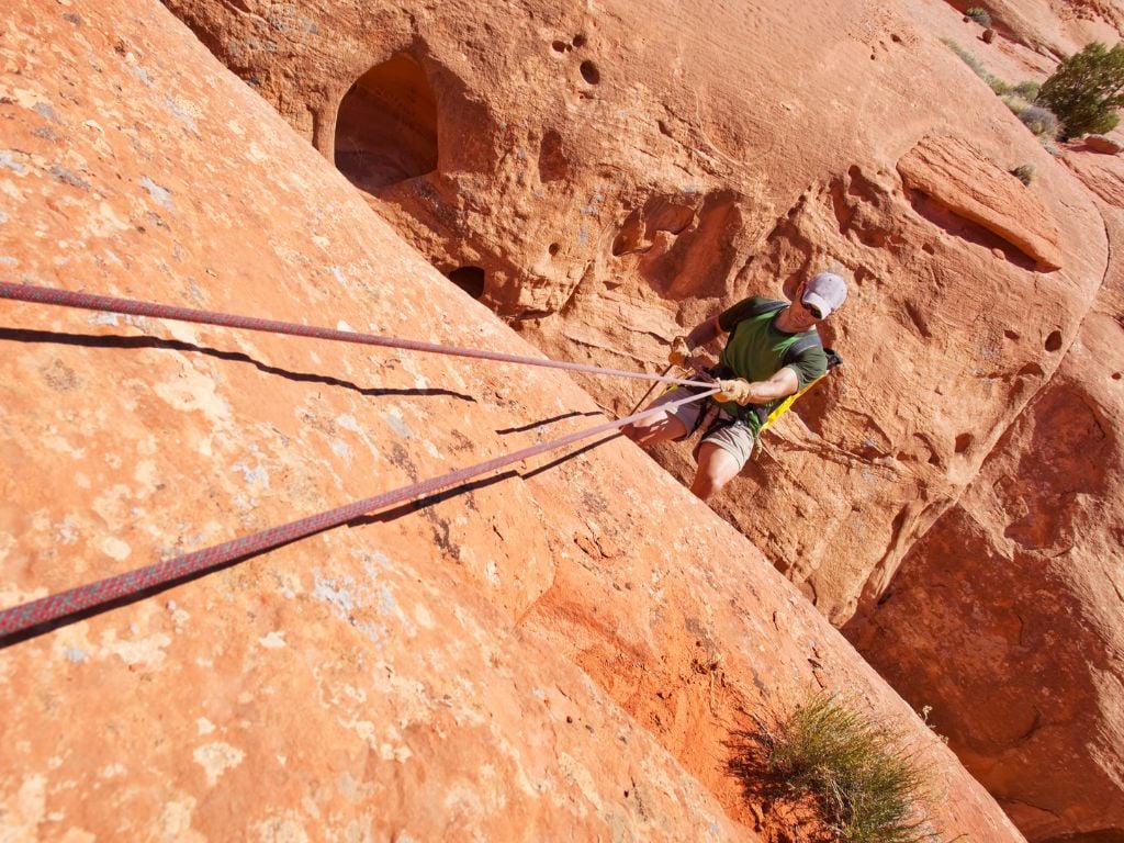 man rappelling down a red rock face in arizona