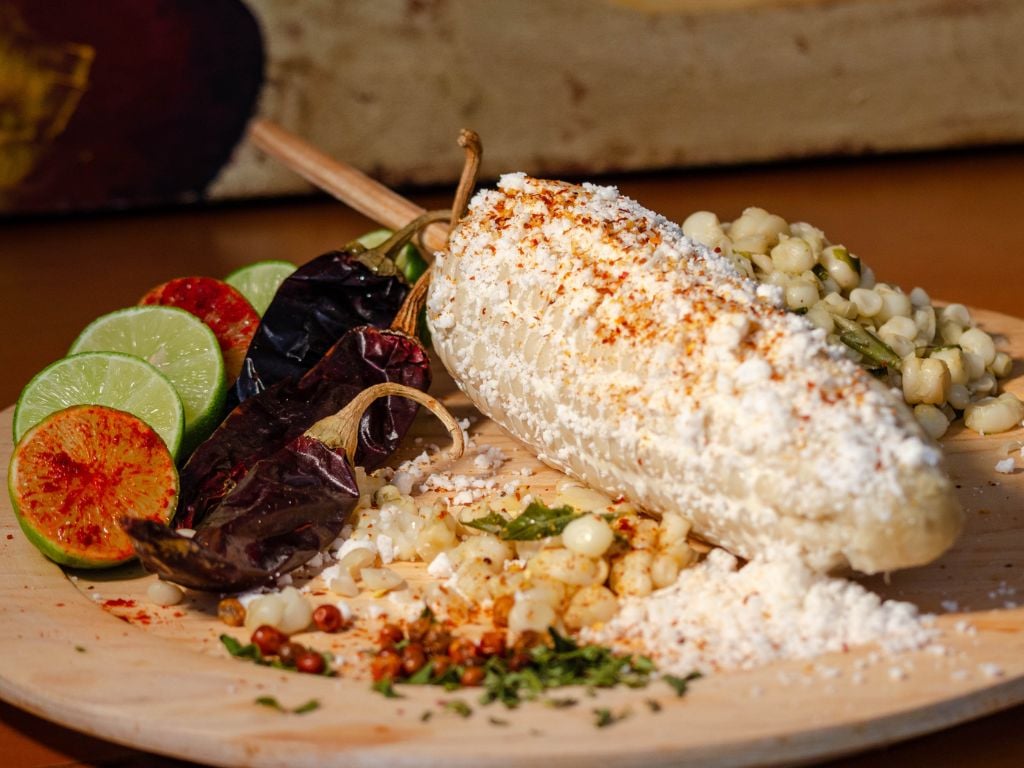 elote corn on a wooden board with lines and hot peppers