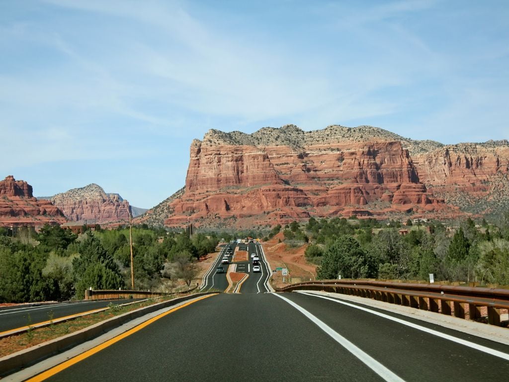 the best way to get around sedona is by a rental car. cars on the highway with mountains behind