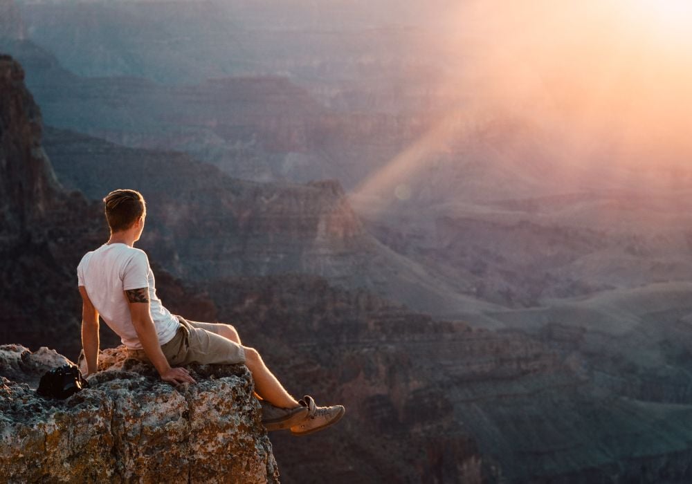 man sitting on the edge of the grand canyon at sunset
