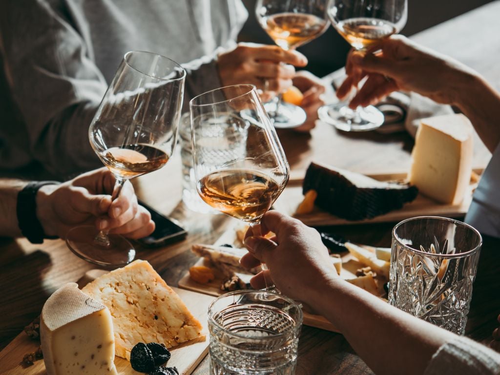 friends cheersing with glasses of wine and a table of cheese