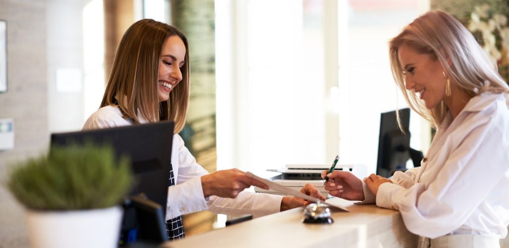 A woman in white communicating with a receptionist 