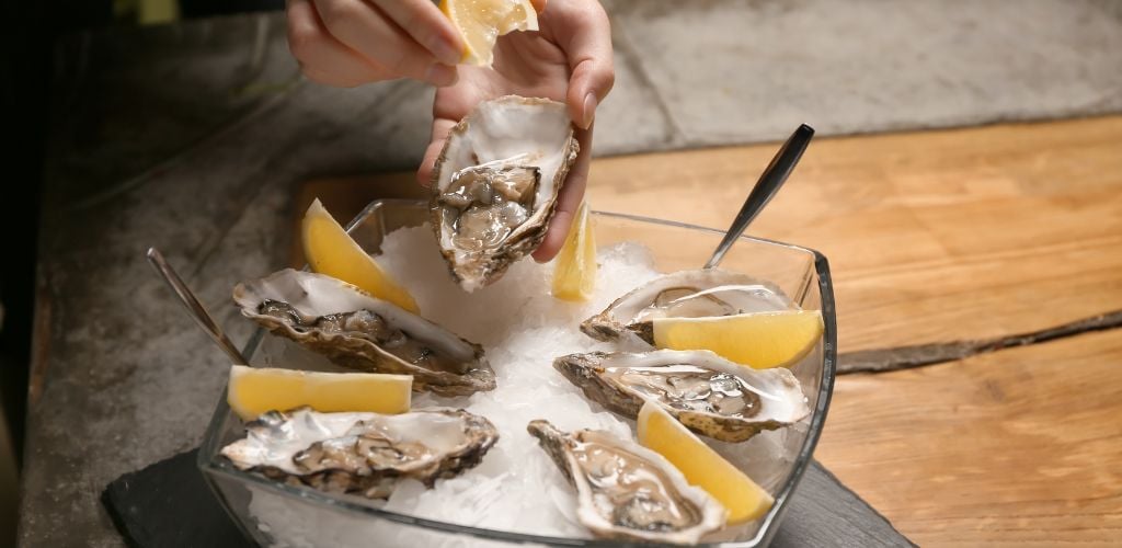 Woman Squeezing Fresh Oysters with Lemon on Table