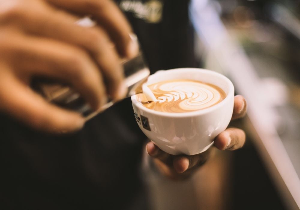 A person holding white ceramic mug filled with cappuccino