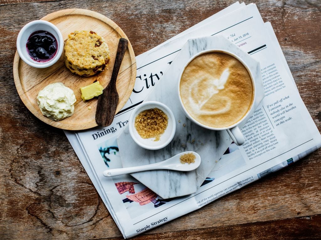 scone with butter and jam and a latte with sugar and a newspaper