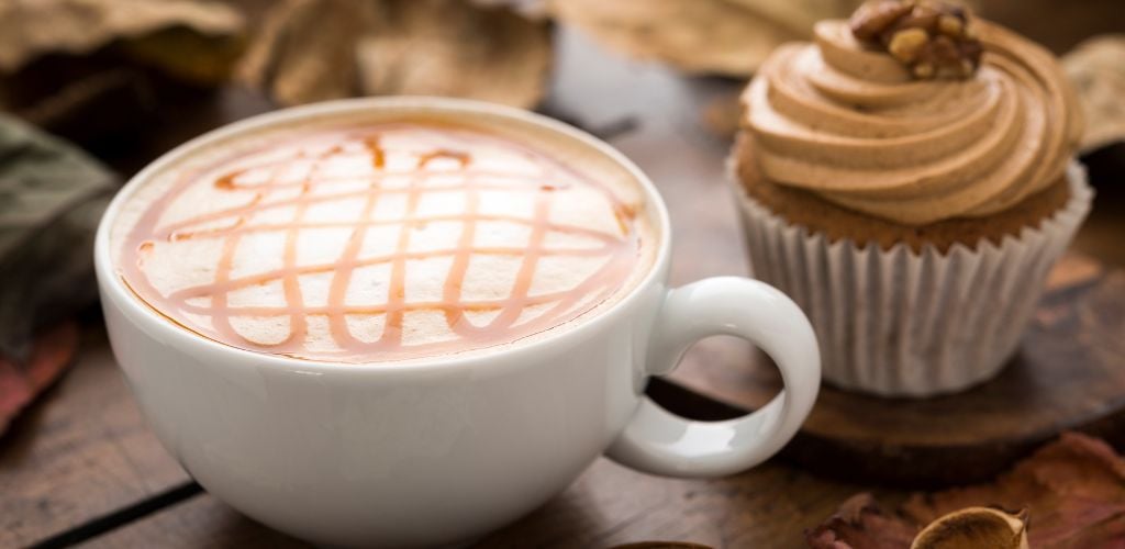 A coffee and a cupcake on the table with dried leaves