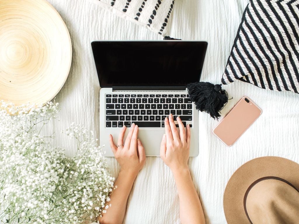 woman with laptop on her bed and hat