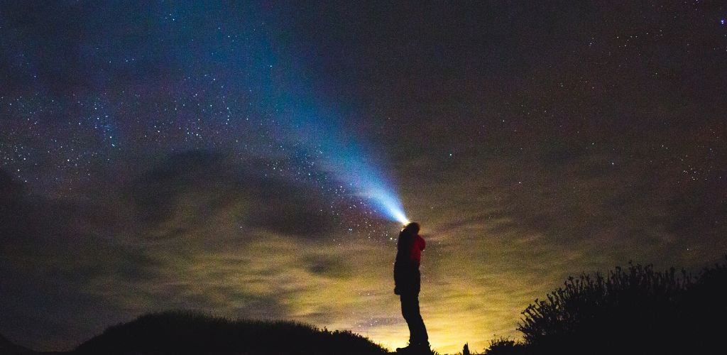 A man pointing flashlight in the sky.