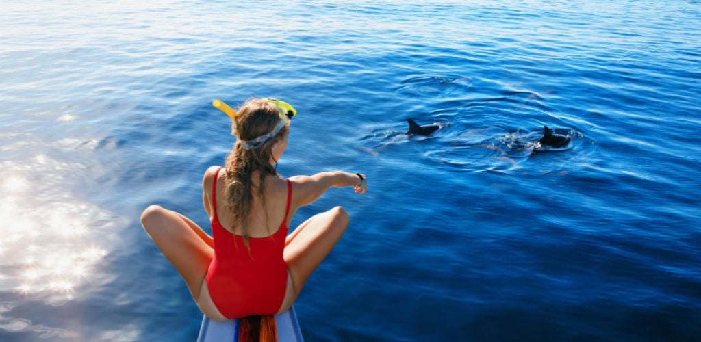 Woman sitting in front of a boat pointing at dolphins 
