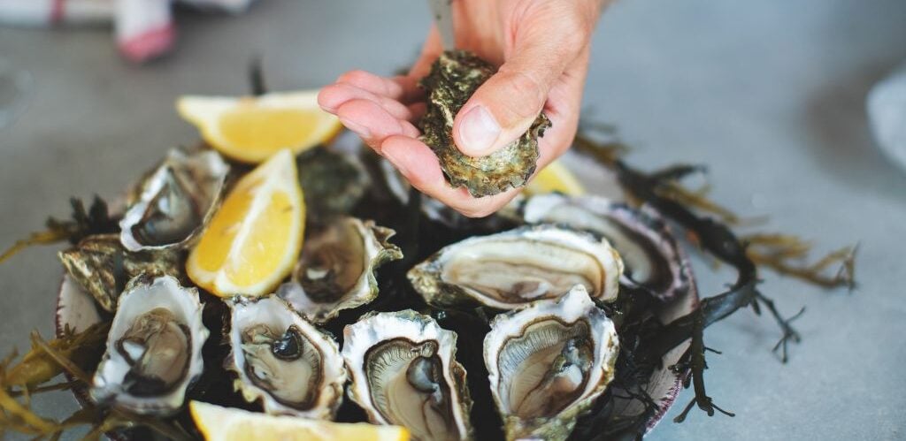 man shucking an oyster with a plate of oysters and lemons
