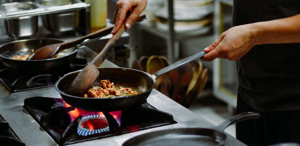 Chef cooking food on a frying pan over gas flame stove