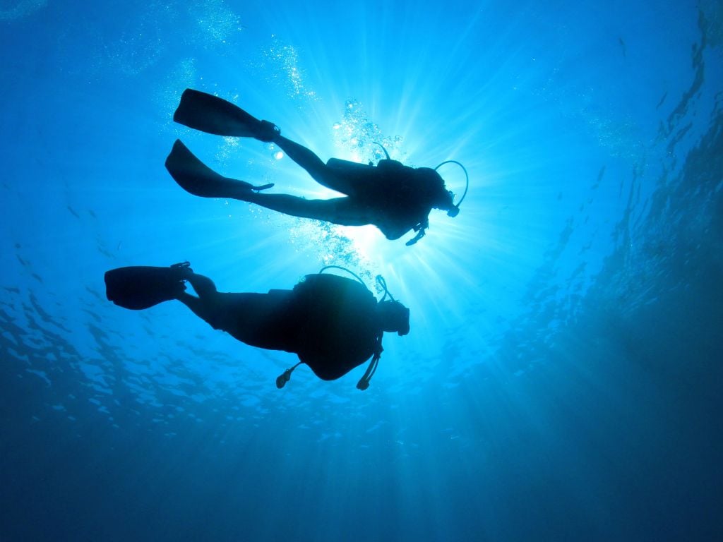 two people scuba diving with sun beaming in from above