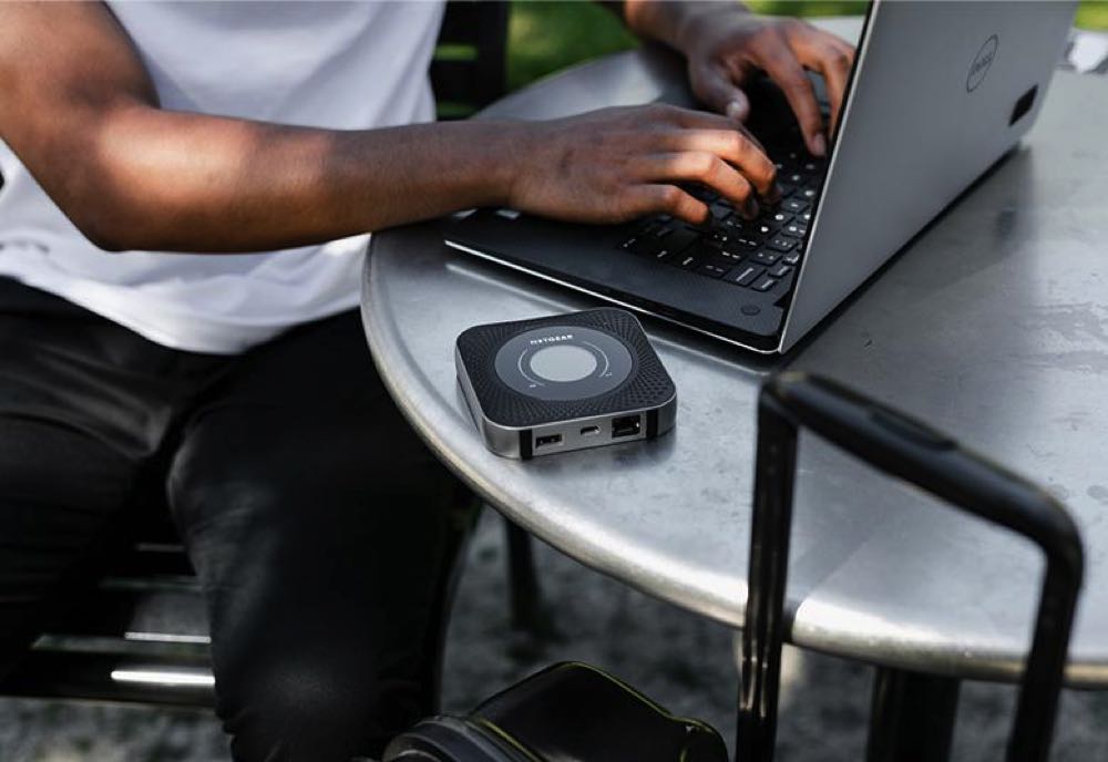 man sitting at a desk typing on a laptop with a travel router on the table