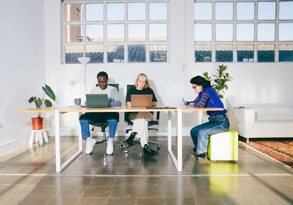 three people working at a desk on their laptops