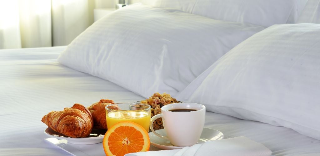 a bread, juice and coffee in the white bed and a white pillow background