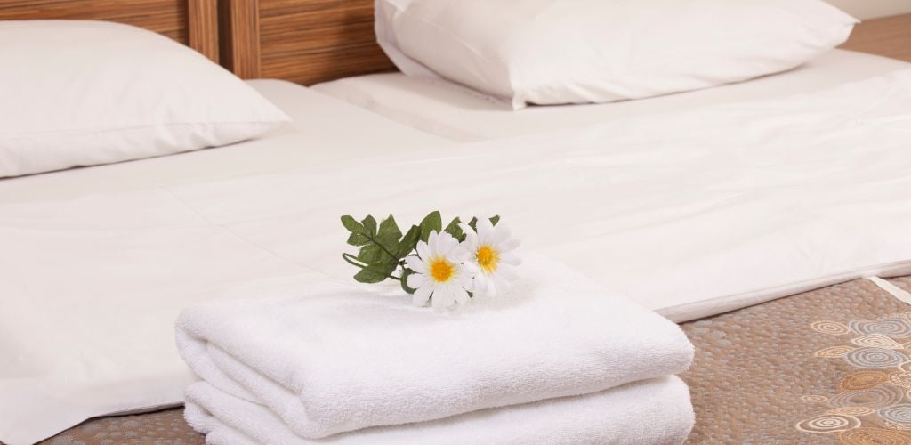 A folded towel place in at the centre of the bed with white flower on top of it