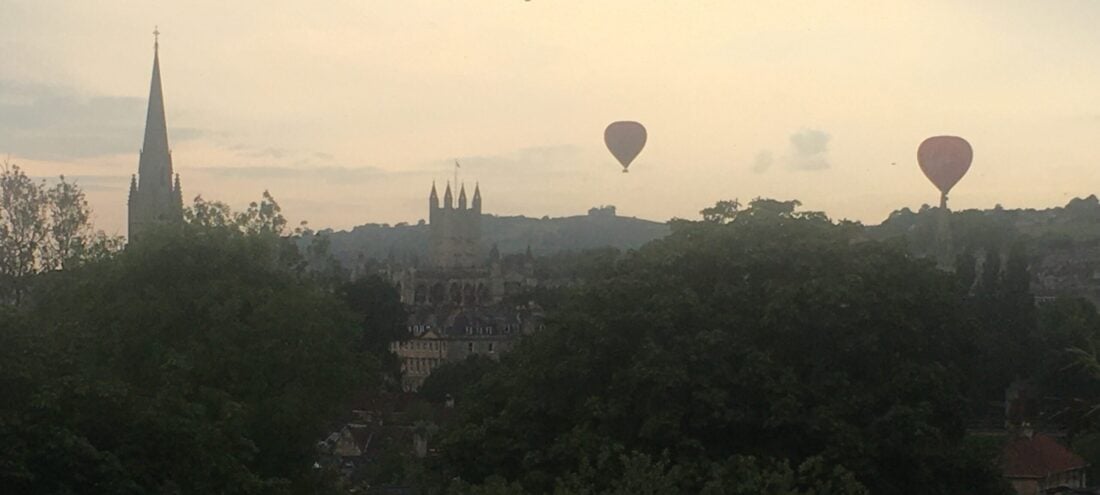 Hot air balloons flying over Bath Abbey and the Bath cityscape.