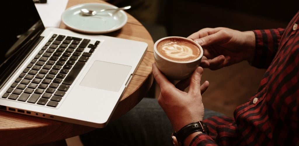 A man hold a cup of coffee and a laptop on the table.
