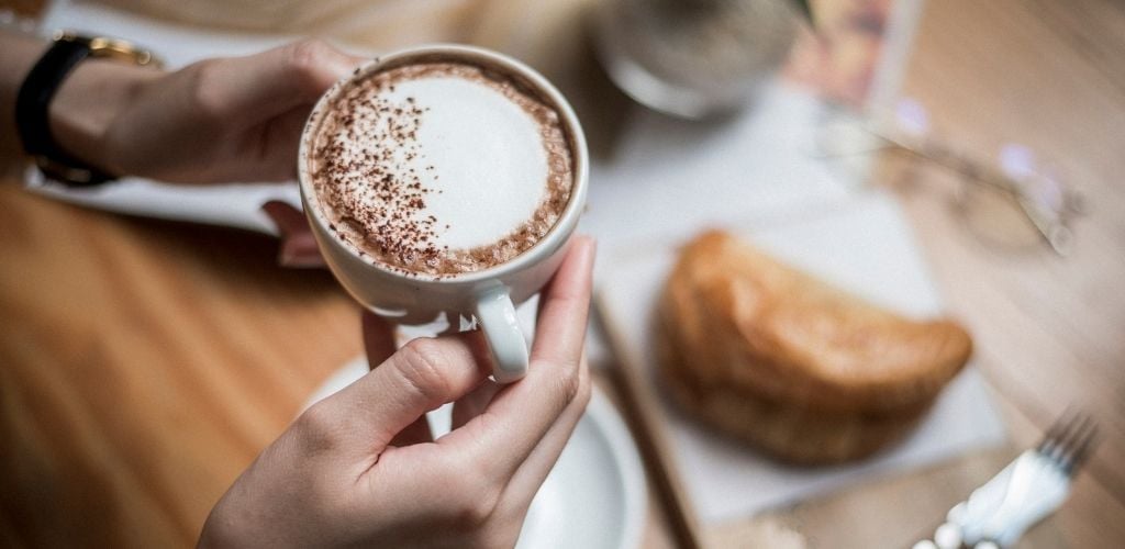 A hand hold a cup of hot coffee and a bread on the table on background.