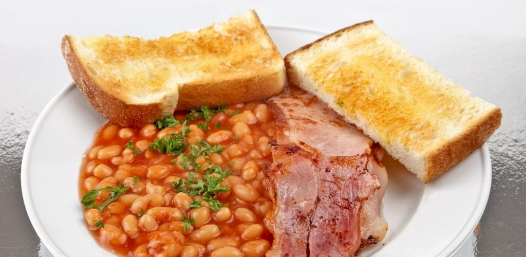 A plate with pork and beans, bacon and two slice of toasted bread. 