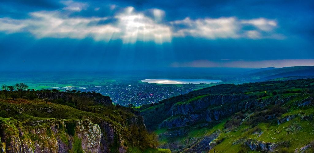 Cheddar Gorge (Somerset) a rocky green mountain covered by a dark blue clouds with lake