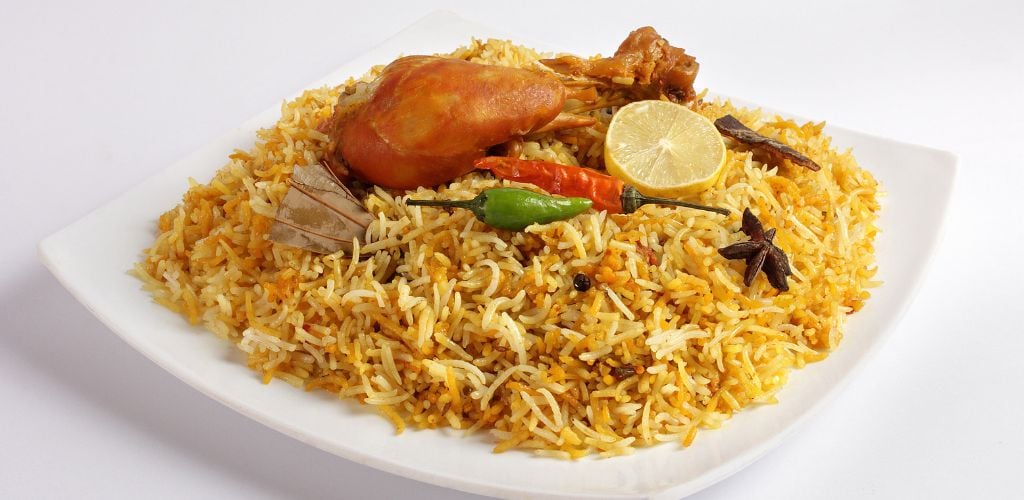 Chicken biryani on a plate. It composing chicken, rice, lemon and chili.
