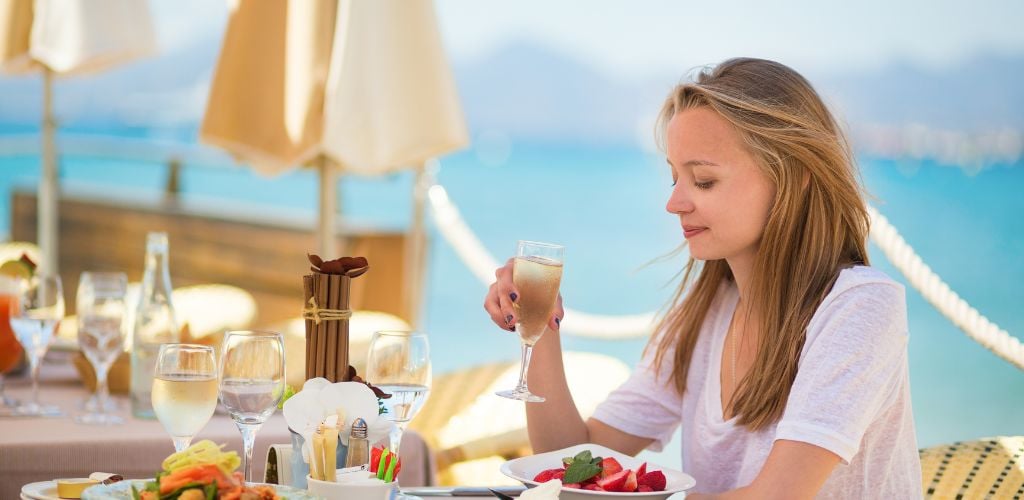 Ocean view restaurant with a woman holding a champagne glass, looking at a bowl of strawberries.