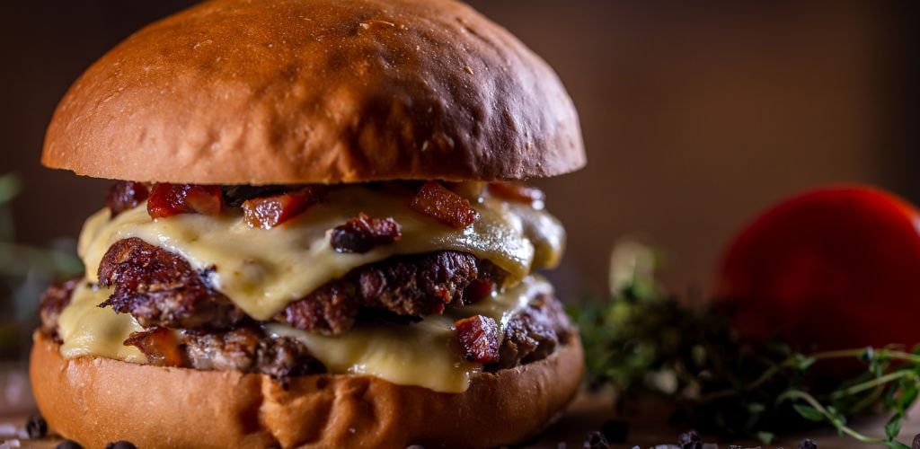 Beef Bacon Burger with melted cheese and a tomato at the background