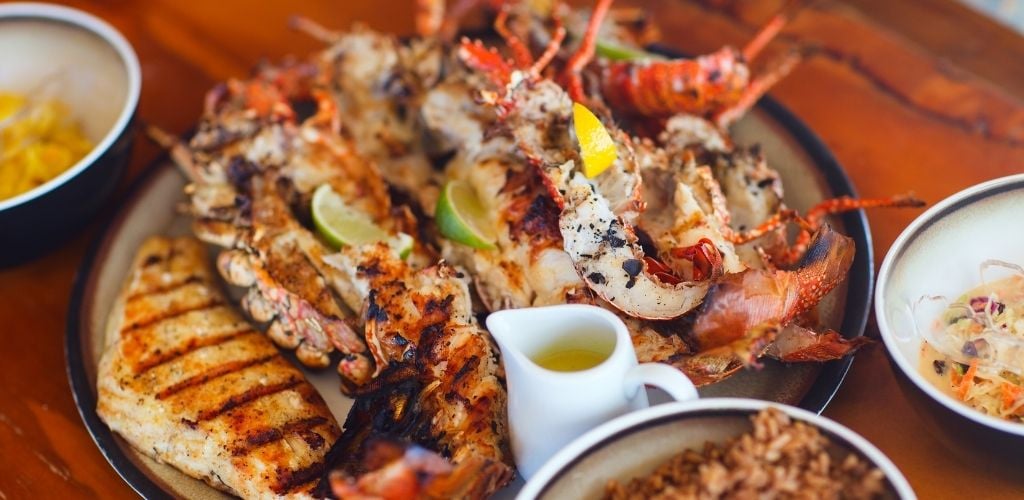 a plate of mixed grilled seafood and lemon juice on the side. other plate has a different variety of foods.